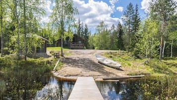 A wooden dock leading to a small wooden cabin surrounded by trees and a calm body of water.