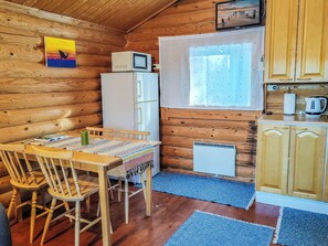 Interior acogedor de una cabaña con una mesa de comedor, sillas, un refrigerador, una ventana con cortinas y armarios de madera.