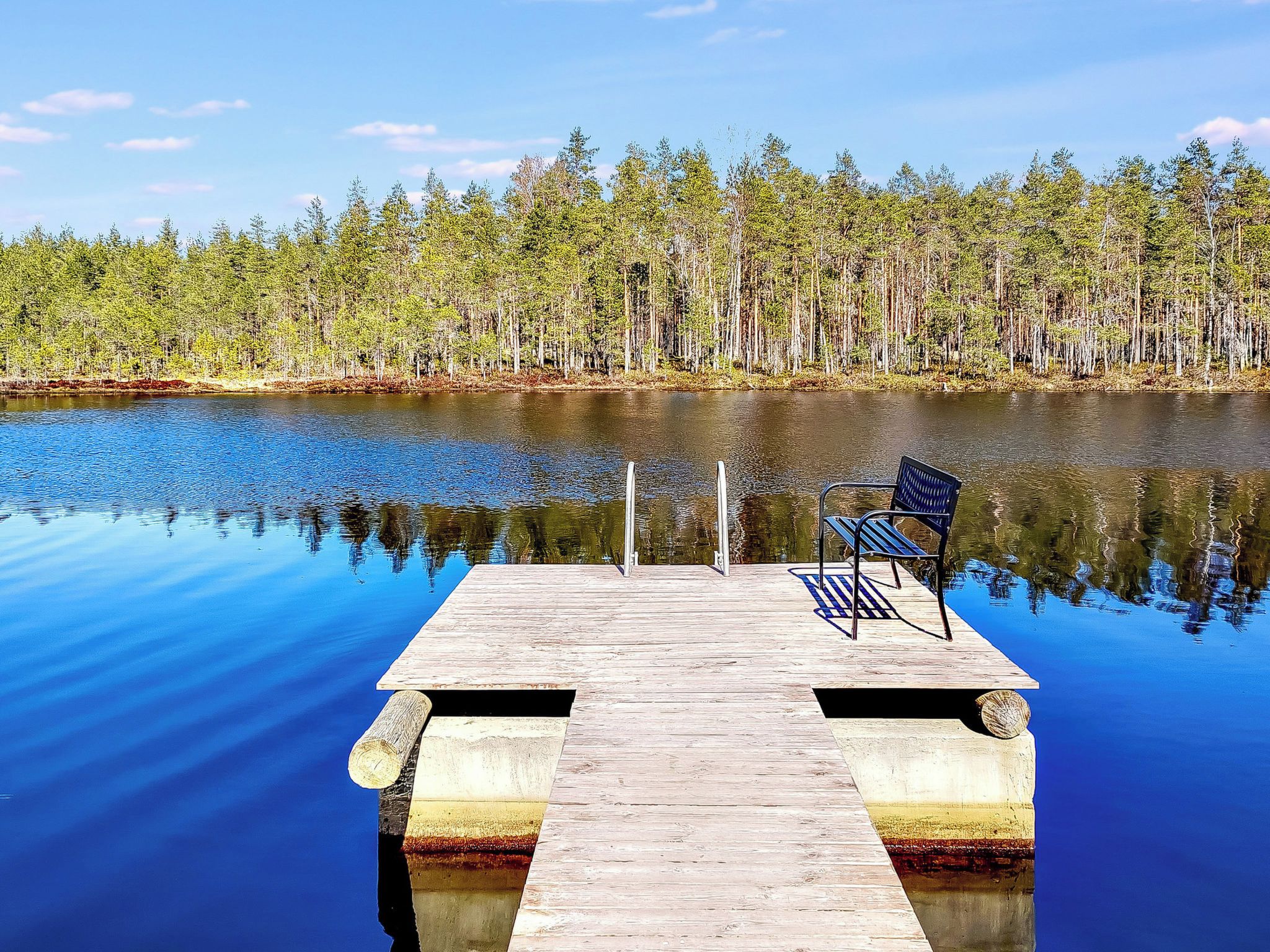A wooden dock extending into calm water with a bench and a metal post.