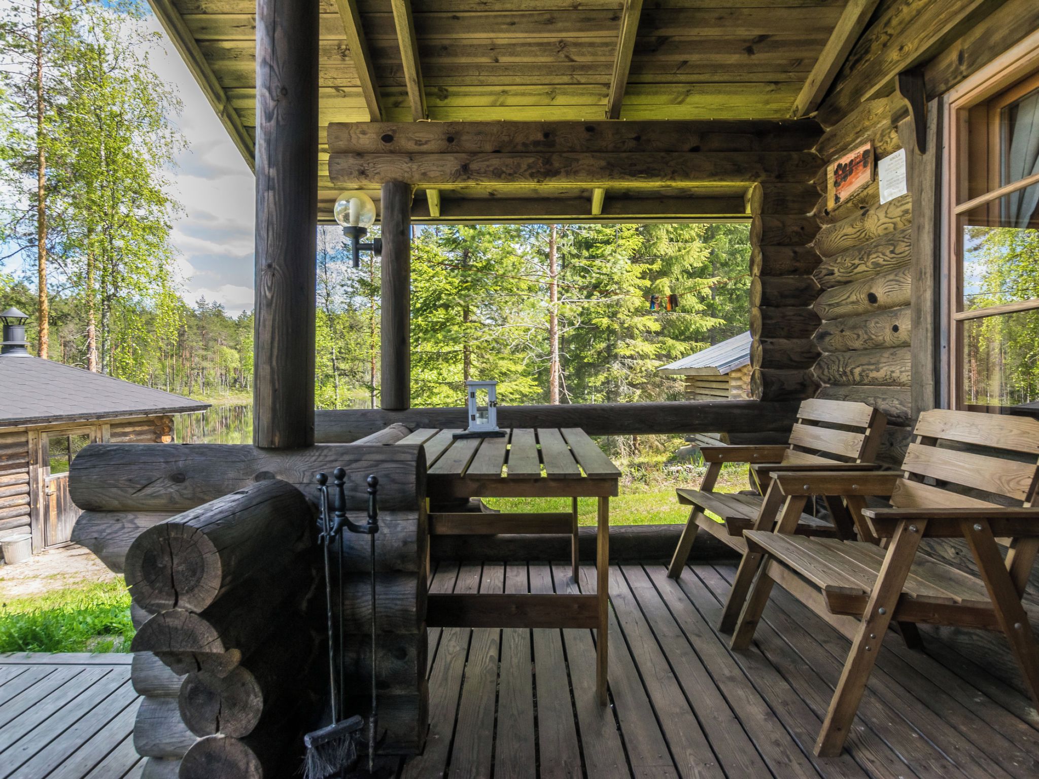 Une terrasse en bois avec une table et des bancs, une lanterne et une pile de bûches.