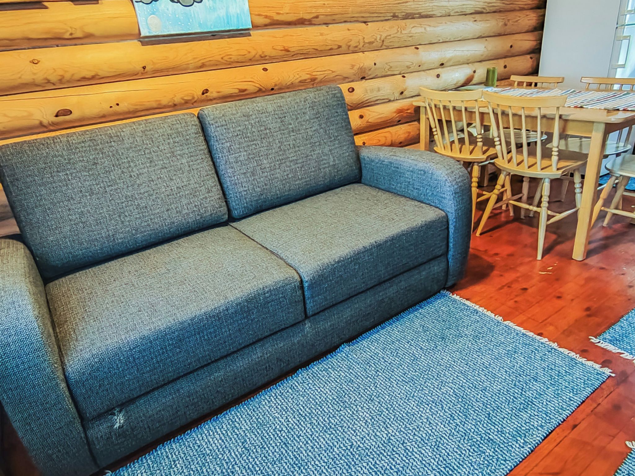 A grey sofa with a blue throw rug in a room with wooden walls and a wooden dining table with chairs.