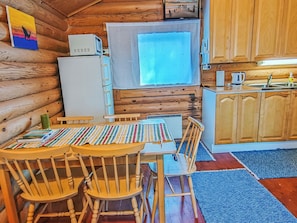 Una cocina acogedora de estilo rústico con paredes de madera, una mesa de comedor con sillas, un refrigerador, un microondas y una ventana.
