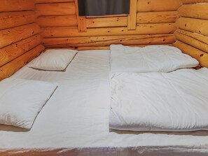 En stuga med träpanel på insidan, med en säng, kuddar och ett fönster.