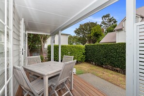 Une terrasse couverte avec une table et des chaises en bois, entourée d’une haie et d’une plateforme en bois.