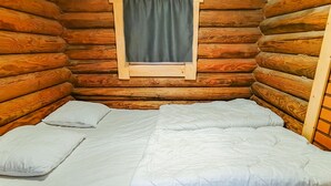 Una cama en una habitación de cabaña de troncos con ventana y paredes de madera.