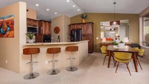 A modern kitchen with a central island, bar stools, and a dining area with yellow chairs.
