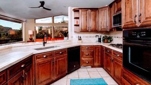 A modern kitchen with wooden cabinets, a black stove, and a large window offering a view of the outdoors.