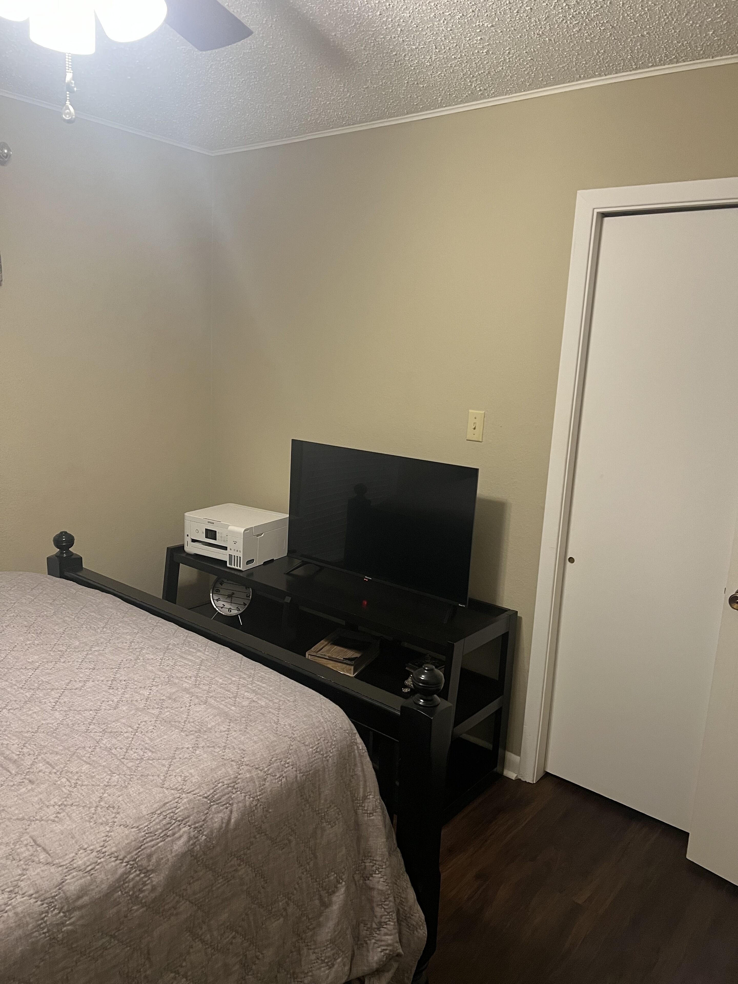 Un dormitorio con una cama, un televisor sobre un mueble, un reloj y una puerta.