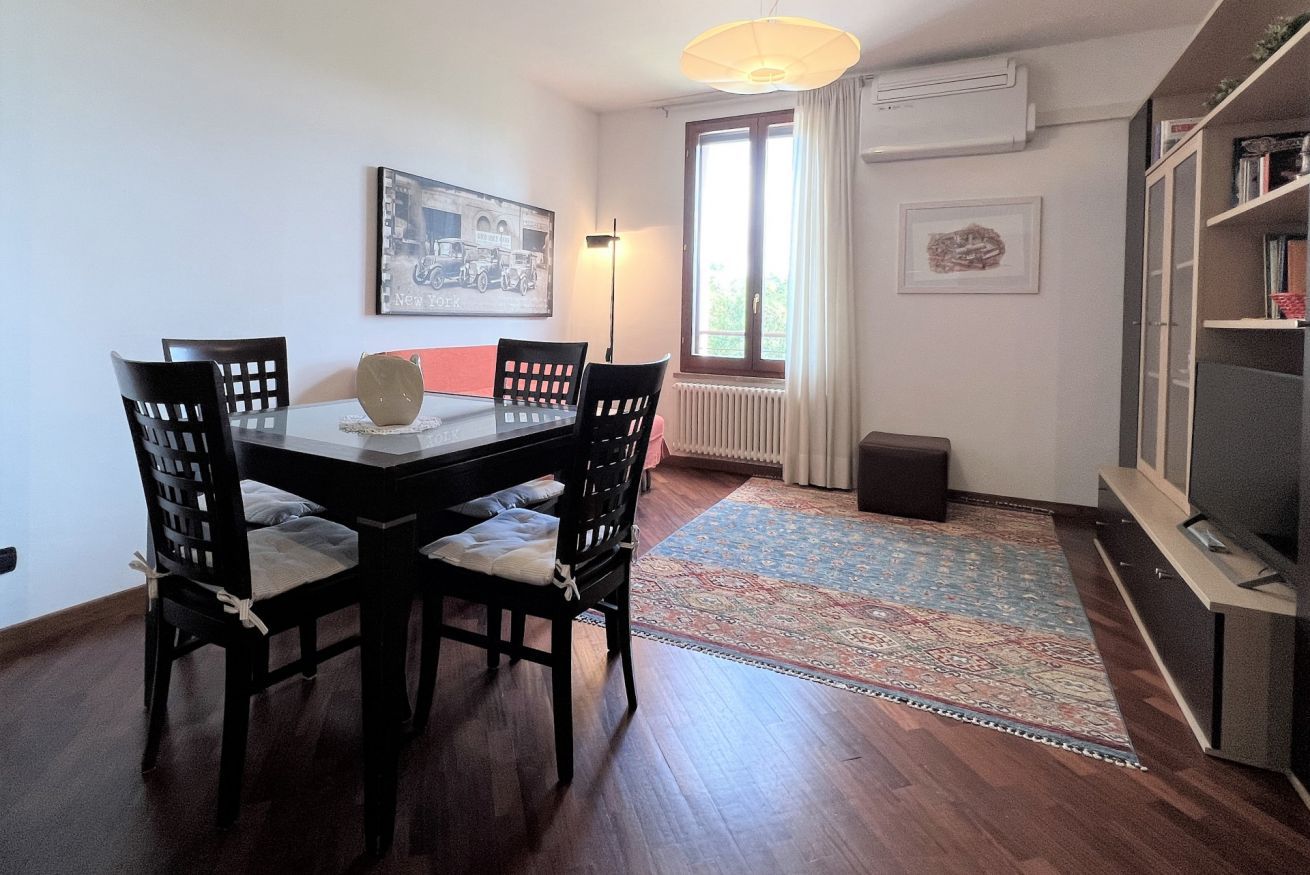 Un comedor con una mesa redonda, cuatro sillas, un jarrón decorativo y una alfombra.