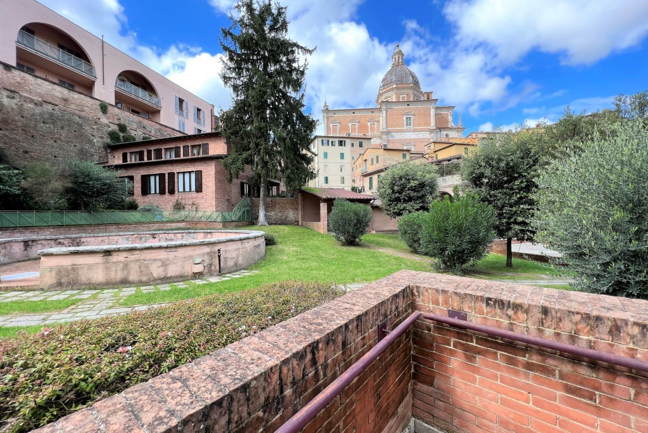 A courtyard with a brick wall, a staircase, and a large tree.