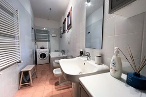 Ein modernes Badezimmer mit einem großen Waschbecken, einer Toilette, einer Waschmaschine und einem kleinen Holzschemel.