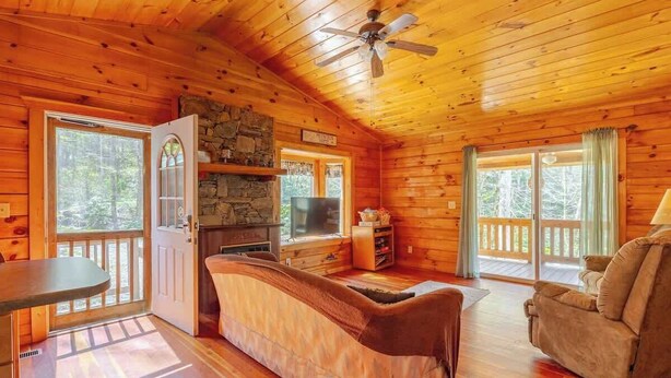 A wooden cabin interior with a stone fireplace, a sofa, a television, and a balcony.
