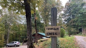 A tranquil creek sign, a wooden cabin, and a gravel path in a forested area.