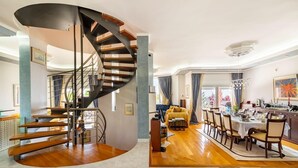 Un amplio espacio habitable con una escalera curva, un área de comedor con una mesa redonda y un rincón de descanso acogedor.