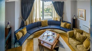 Un salón con un sofá azul curvo, una mesa de centro de cristal y vistas a un jardín a través de amplios ventanales.