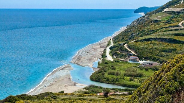 Un paisaje costero con una carretera serpenteante, una playa y un pequeño asentamiento con edificios.