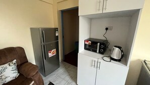 A compact living space with a sofa, a refrigerator, a microwave, and a kettle.