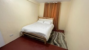 A small, single-bed room with a wooden headboard, a striped rug, and a brown floor.