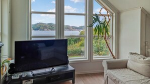 Ein Wohnzimmer mit einem großen Fenster, das Blick auf ein Gewässer und Hügel bietet.