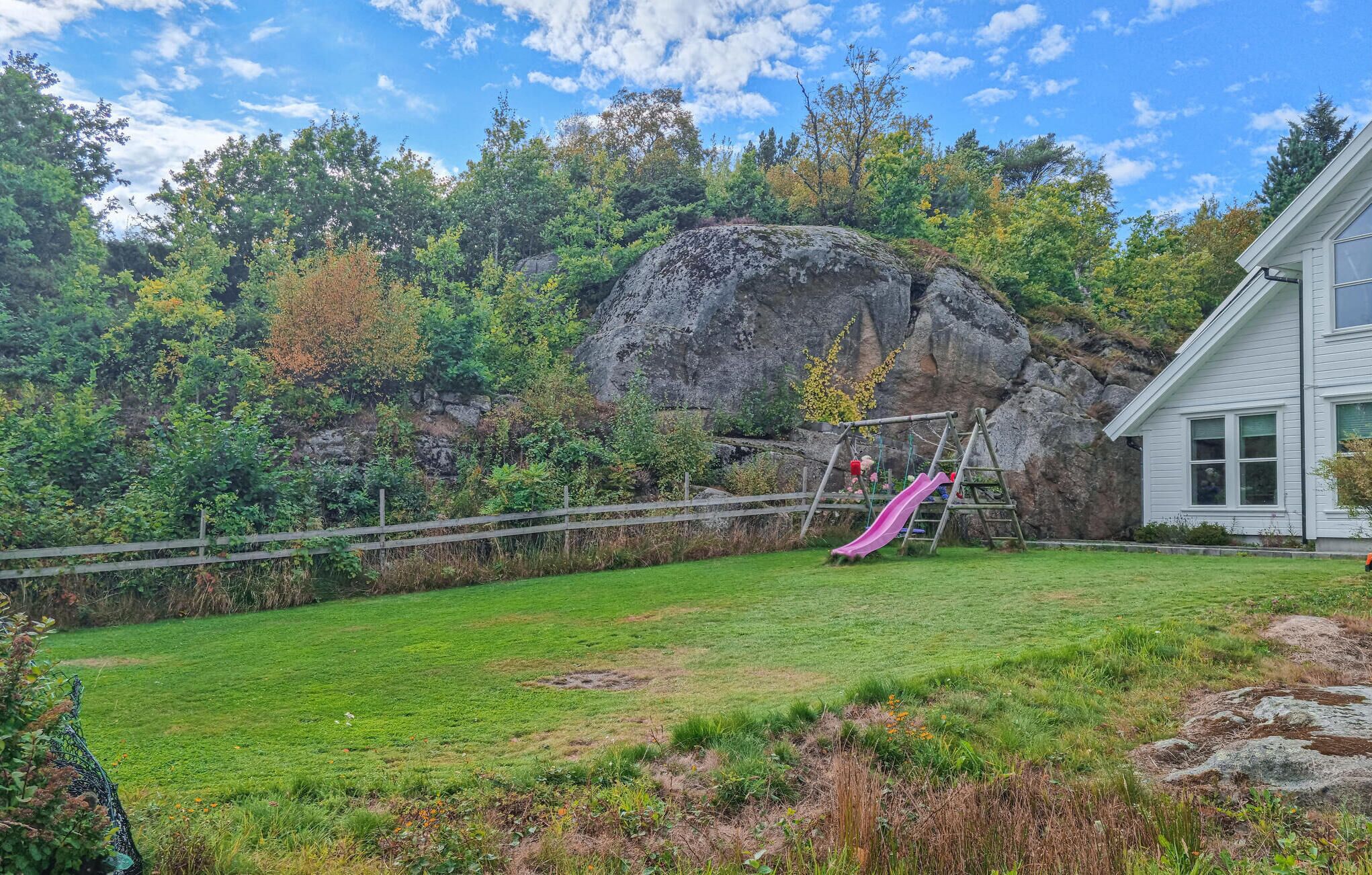 A backyard with a swing set, a rock formation, and a house.