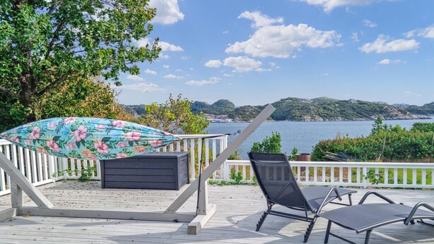 Eine Terrasse mit Hibiskus-Sonnenschirm, einem schwarzen Stuhl und einer Bank mit Blick auf einen See und sanfte Hügel im Hintergrund.