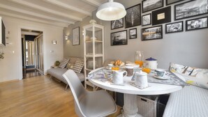 A dining area with a round table, chairs, and a white pendant light. There are framed pictures on the wall and a white shelving unit. - Santo Spirito Romantic by Mmega (Firenze)