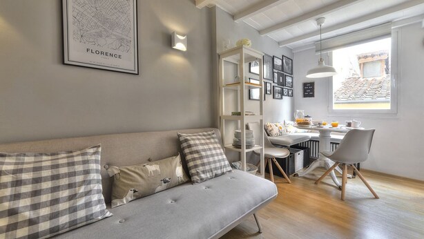 A modern living room with a grey sofa, a dining area, and a window with a view. - Santo Spirito Romantic by Mmega (Firenze)