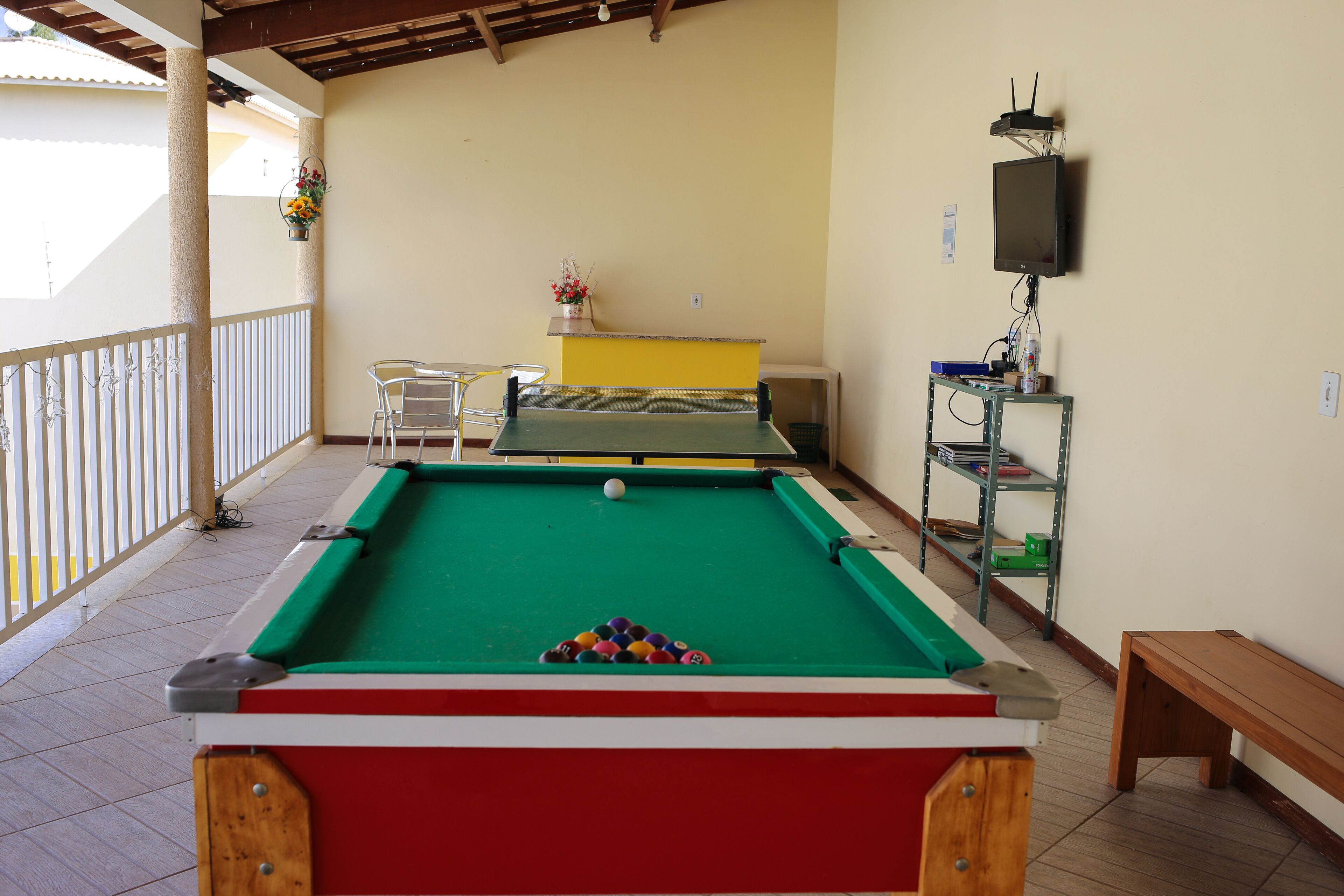Una mesa de billar con bolas, un banco y una mesa de tenis de mesa en una habitación con balcón.