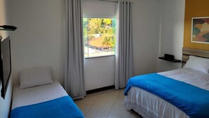 Habitación de hotel con dos camas, ventilador de techo, ventana con cortinas y vista a espacios verdes.