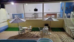 Un área de piscina interior con una piscina pequeña, sillas de plástico blancas y sombrillas.