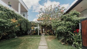 A narrow stone pathway leading to a covered entrance surrounded by lush greenery and potted plants. - Dana's House (Tabanan)