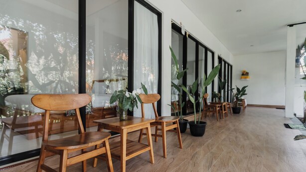 A spacious indoor area with wooden chairs and tables, large windows with curtains, and potted plants. - Dana's House (Tabanan)