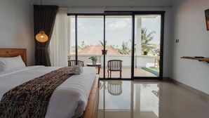 A hotel room with a large bed, a balcony with chairs, a small table, and a view of palm trees. - Dana's House (Tabanan)