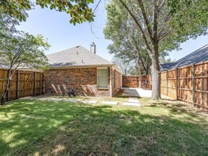 Stroll through the serene backyard, surrounded by lush greenery and a charming brick house with a chimney.