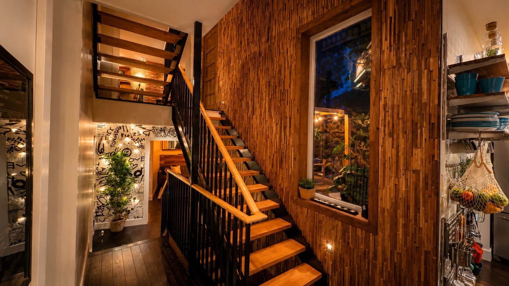 Una escalera de madera con vistas al exterior, un área de cocina con estantes y un ventanal con vistas panorámicas.