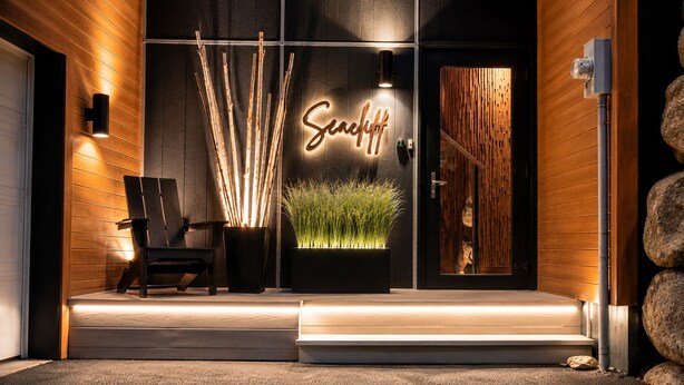 A modern building entrance with a wooden facade, a neon sign, a chair, and a planter with grass. - Seacliff- Luxury Halifax Waterfront Paradise -Pool, Hot Tub, Wharf & Boathouse (Halifax)