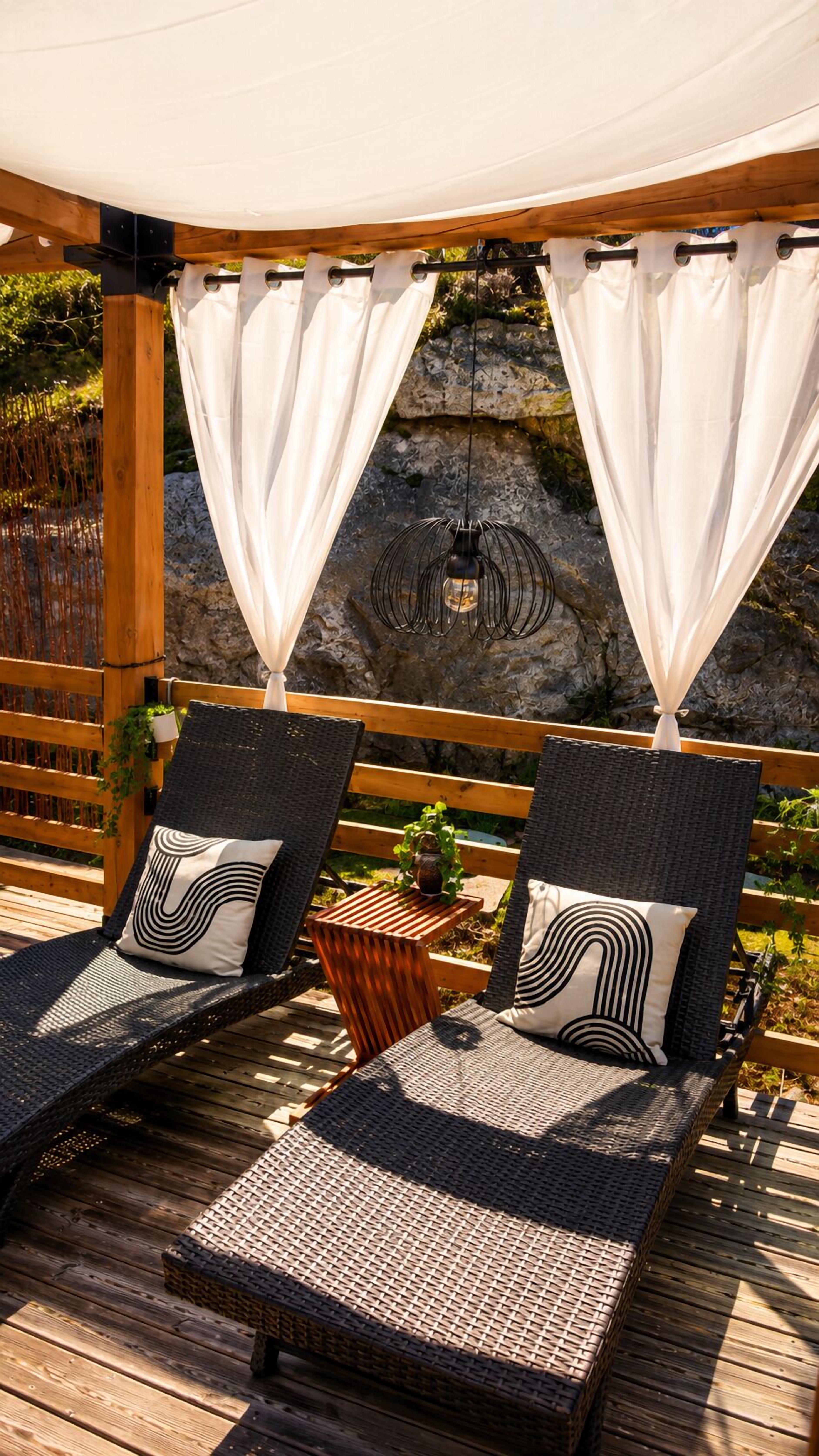 Two wicker lounge chairs with black and white patterned cushions, a small wooden table with a plant, and a hanging light fixture.