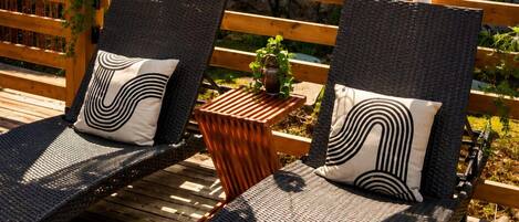 Two wicker lounge chairs with black and white patterned cushions, a small wooden table with a plant, and a hanging light fixture.