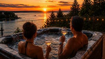 Two individuals in a hot tub with a sunset view over a body of water.