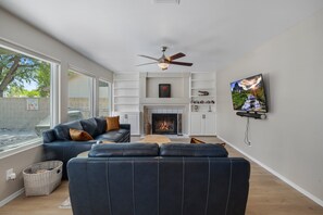 Una sala de estar moderna con chimenea, ventilador de techo y televisor montado en la pared.