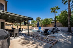 Un espacio exterior techado con piscina, sillas de descanso y zona de barbacoa.