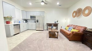 Una cocina moderna con armarios blancos, electrodomésticos de acero inoxidable y una zona de comedor con sofá de cuero marrón y una mesa de centro.