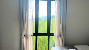 A room with a large window, a bed with a patterned bedspread, and a white pillow.