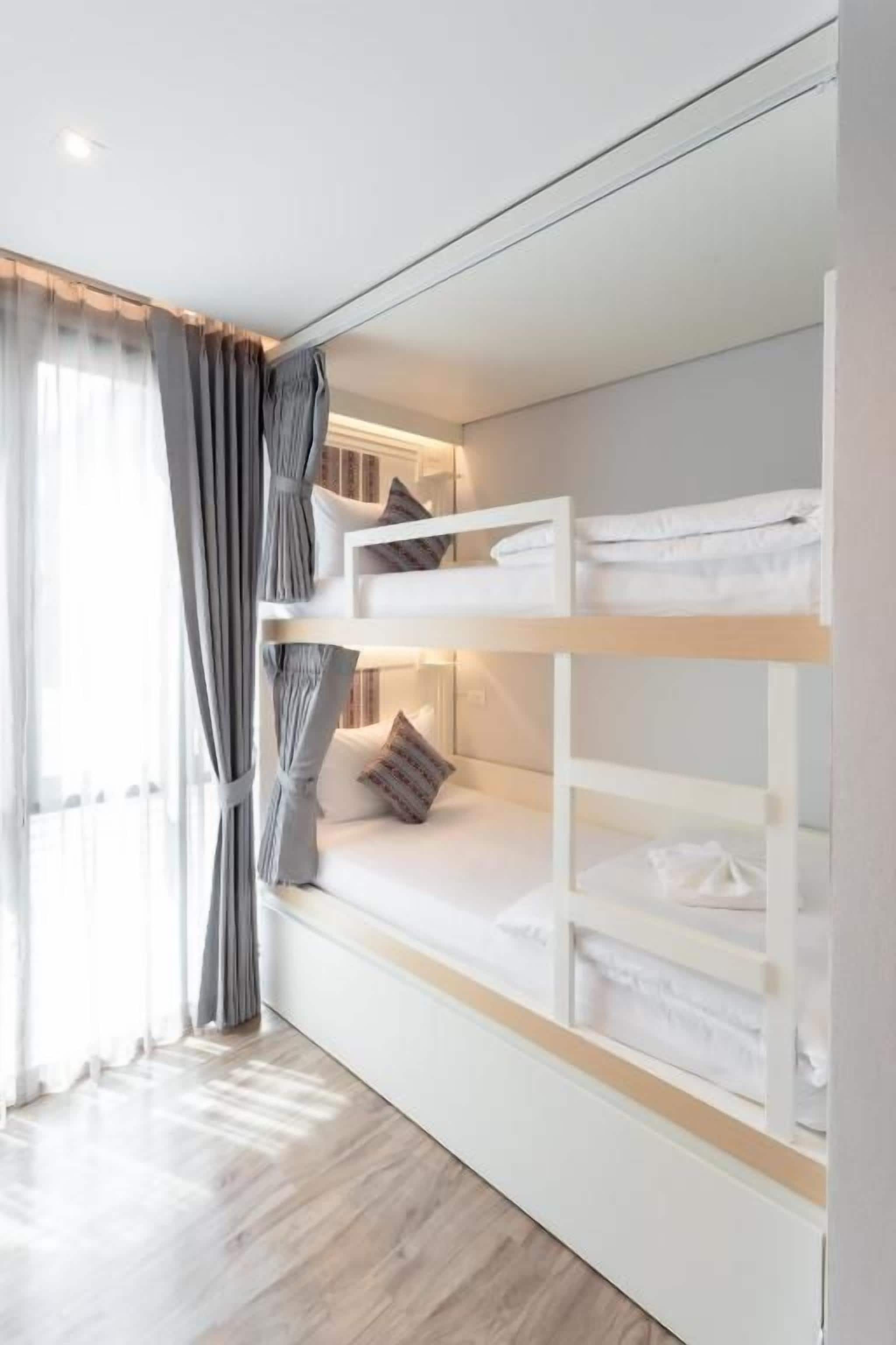 A bunk bed with white bedding and a window with curtains.