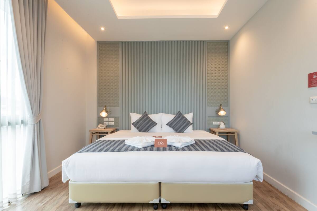A modern hotel room with a large bed, a bedside table with a lamp, and a wall-mounted light fixture.