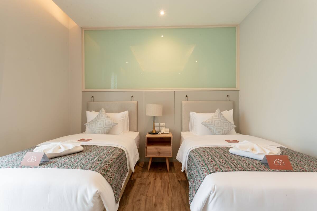 A hotel room with two beds, a nightstand, and a large window.