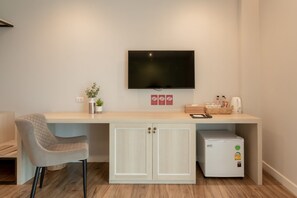 A modern room with a flat-screen TV mounted on the wall, a light-colored desk with a chair, a small refrigerator, and a potted plant. - Lanna Bonita Boutique Hotel (Chiang Mai)