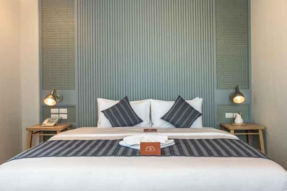 A neatly made bed with a striped bedspread, two pillows, and a bedside table with a lamp and a phone.