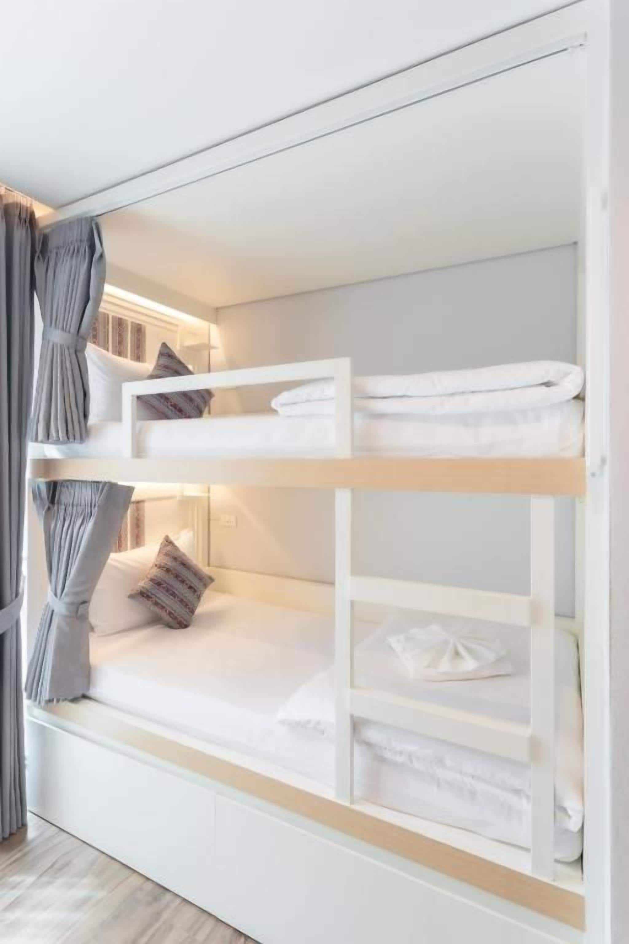 Uma cama beliche com roupa de cama branca e uma cortina do lado esquerdo.