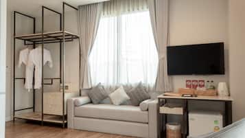 A modern hotel room with a sofa, a TV, a wardrobe, and a small kitchenette.